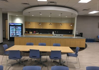 Wooden cabinets installed by MAC in a large breakroom with blue chairs and brown tables