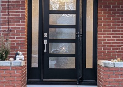 Dark wood door with frosted glass accents built into a brick house