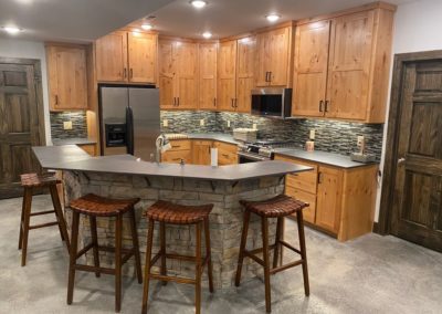 Dark wood cabinets made by MAC under black marble countertop with silver appliances and barstools