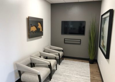 Waiting area with three chairs and light wood flooring with a TV on the wall