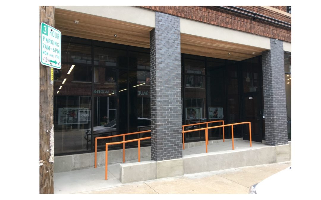 Stone accessibility ramp with orange rails into a windowed office building