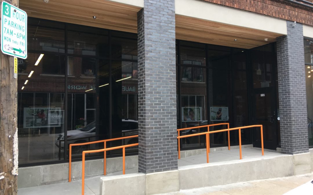 Stone accessibility ramp with orange rails into a windowed office building