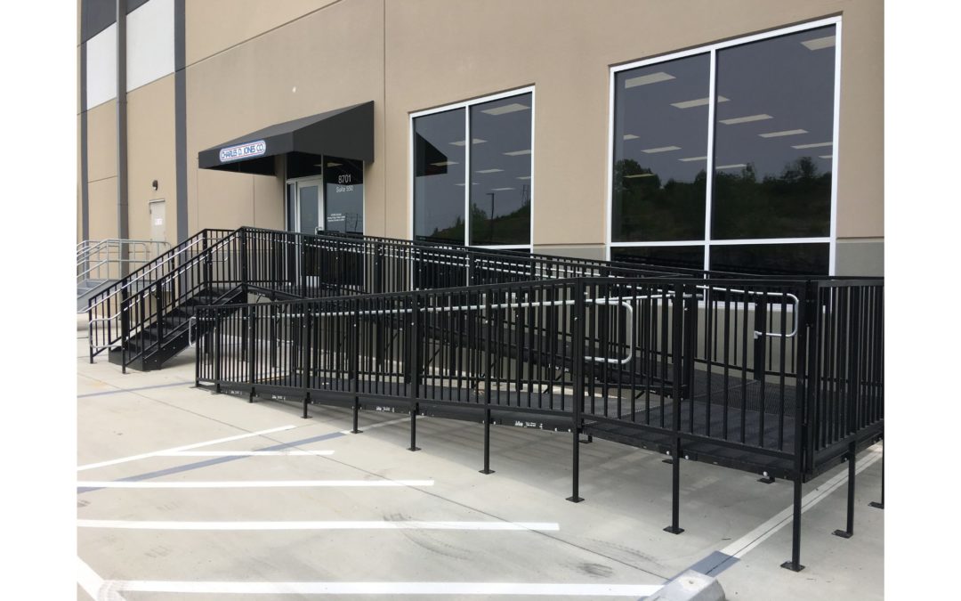 Black iron stairs and accessibility ramp leading into a large tan building